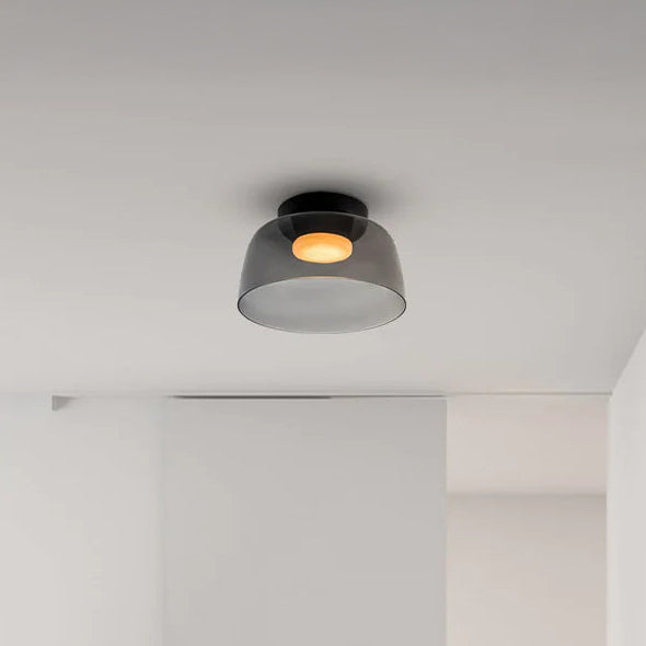 Smoked acrylic flush mount light with a compact drum shade and warm circular glow in a minimal white interior.