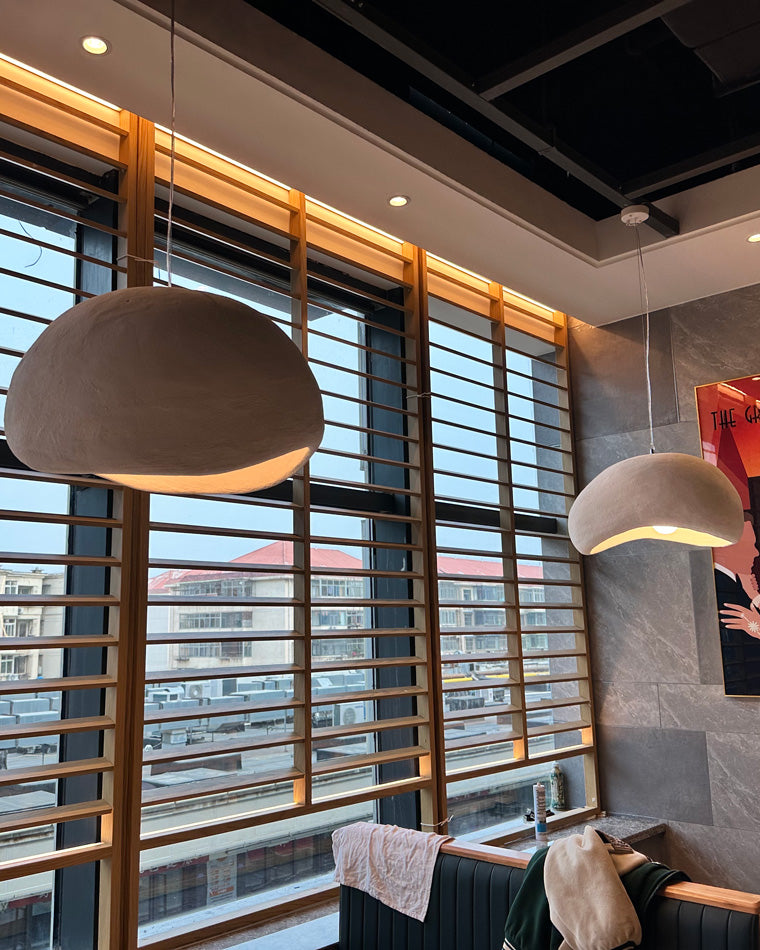 A grey dome pendant glows beside horizontal wood blinds in a warmly lit restaurant interior.