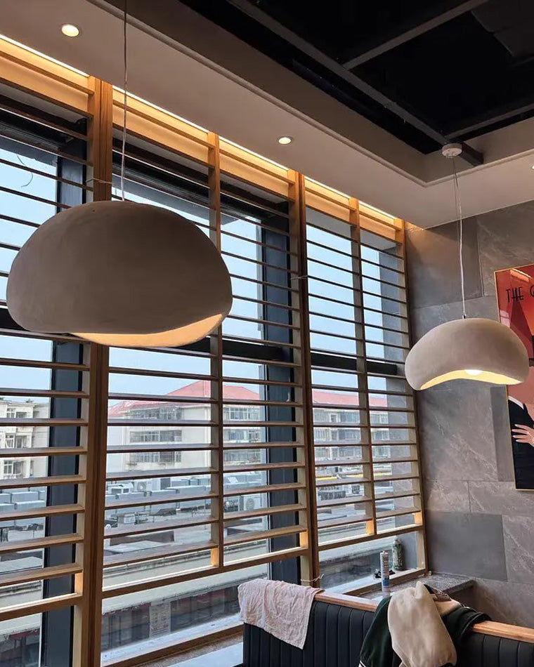 A large grey dome pendant glows warmly beside wood blinds, highlighting its textured outer surface.