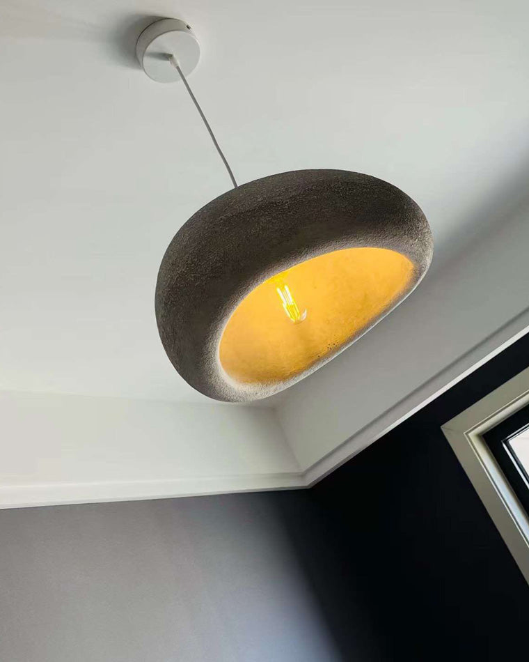 Low-angle detail of a grey pendant revealing its granular resin texture and warm inner surface.
