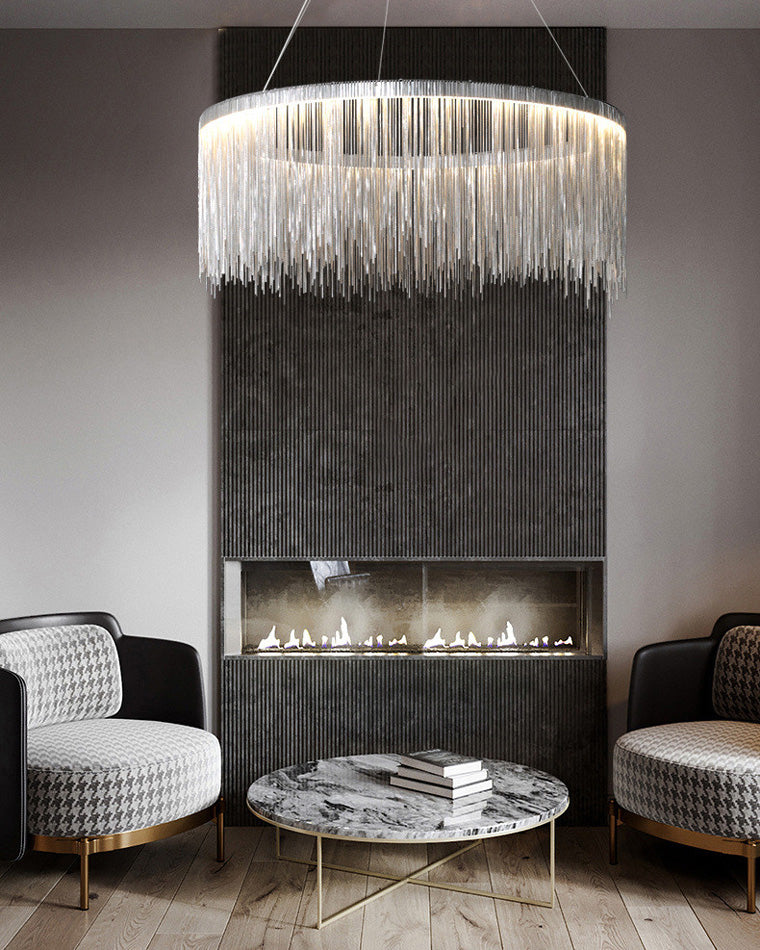 Silver waterfall chandelier shimmering above a marble coffee table and dark fireplace, lifting the moody lounge with movement and reflected light.