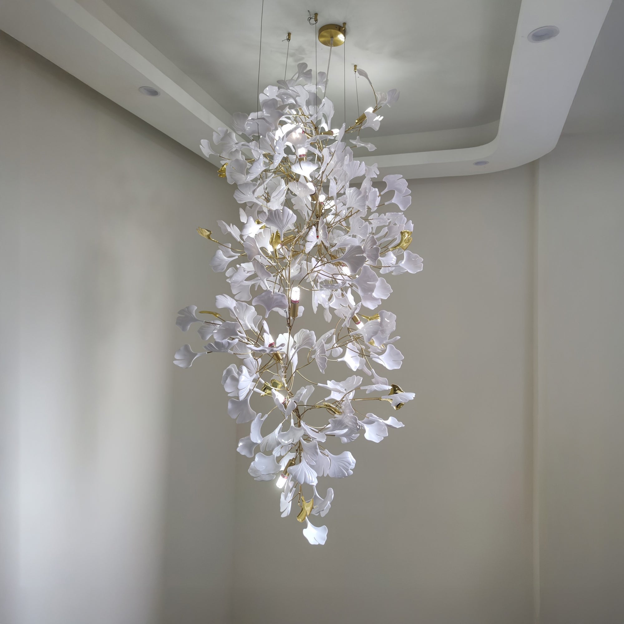Ceramic ginkgo foyer chandelier with a round gold-toned canopy and slim suspension wires, shown illuminated in a tall interior.