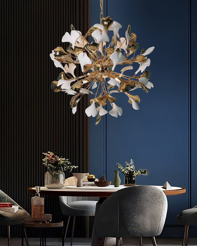 Close-up of a modern dining area with a wooden table and gray chairs; a detailed view of a white and gold ginkgo leaf chandelier suspended above the table is highlighted.