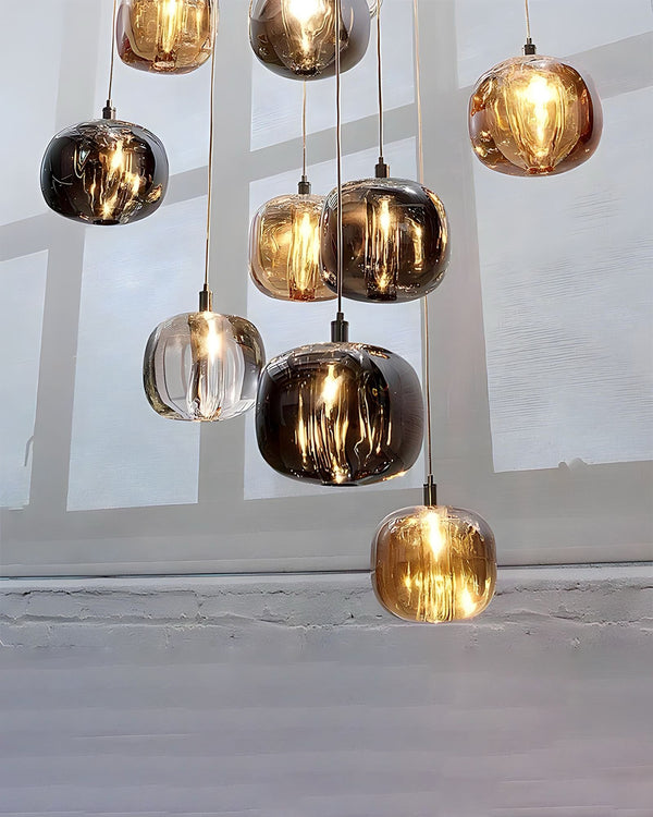 Close-up of glowing amber, smoked, and clear glass pendants on the glass chandelier, showing the warm layered look of the waterfall cluster beside a window ledge.