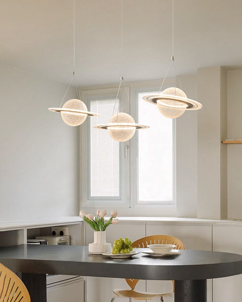 Three glowing planet pendants create a globe chandelier above an oval black dining table in a bright minimalist room.