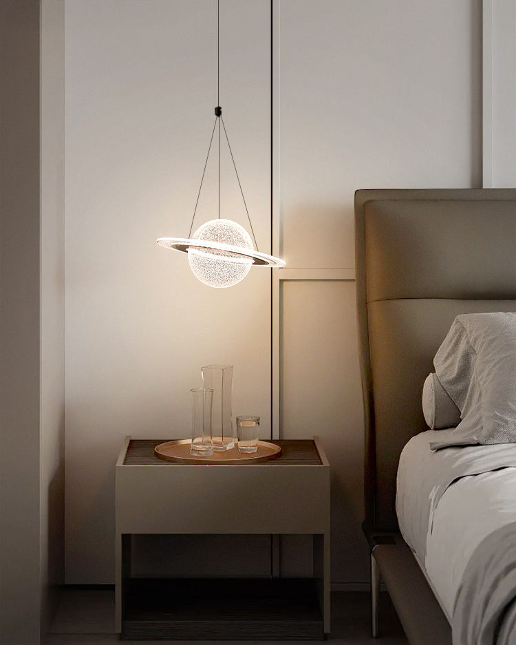 Compact globe pendant with a luminous orbit ring hanging above a bedside table beside a gray upholstered bed.