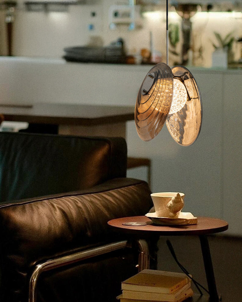 Warm-lit glass disc pendant light beside a headboard and books, highlighting a cozy reading-corner mood.