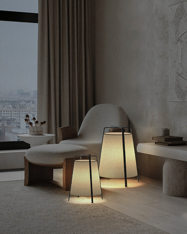Two beige paper lantern lamps in small and large sizes styled beside a lounge chair in a calm living room corner.