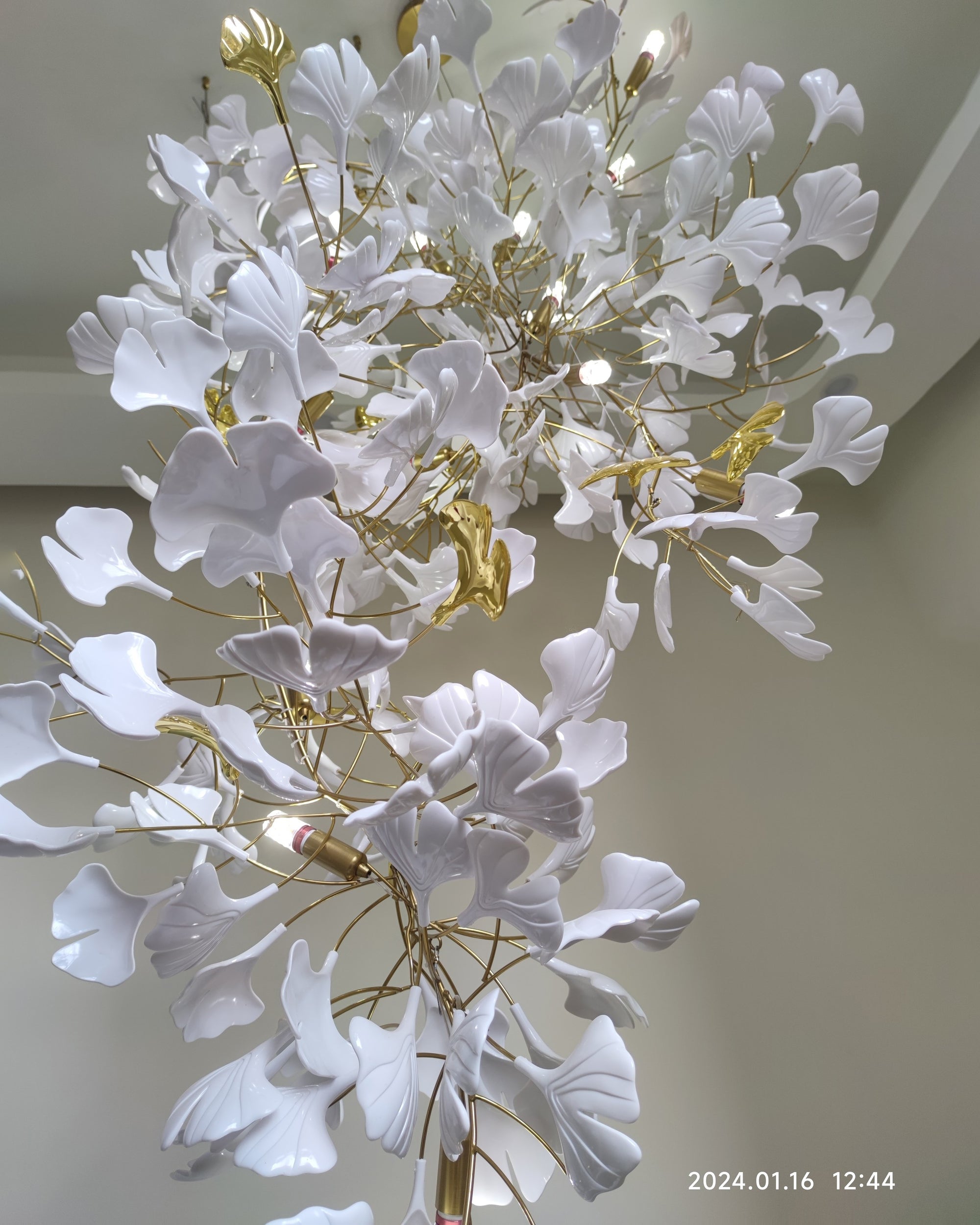 Leaf chandelier close-up showing glossy white ceramic ginkgo leaves, gold-toned brass branches and visible G9 bulbs.
