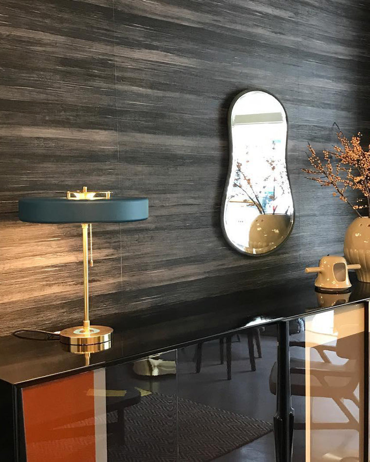 Blue modern table lamp glowing on a glossy black console beneath an organic-shaped mirror and ceramic vases.