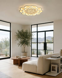 Illuminated flush mount ceiling light with a layered flower silhouette and crystal center in a bright modern living room with black-framed windows.