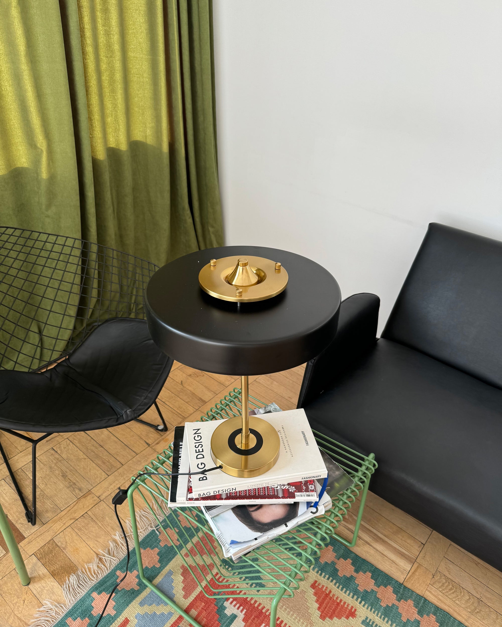 Black vintage desk lamp viewed from above on a green wire side table stacked with design books between black chairs.