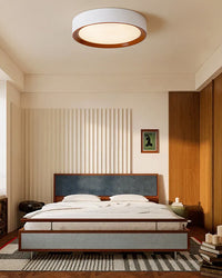 Modern flush mount ceiling light centered above a low platform bed with walnut wall accents.