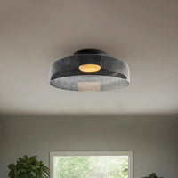 Wide smoked acrylic flat ceiling lamp with a low-profile round shade and warm light above a window and indoor plant.