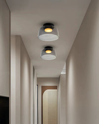 Two smoked acrylic hallway ceiling lights with compact drum shades and warm circular glows along a narrow modern corridor.