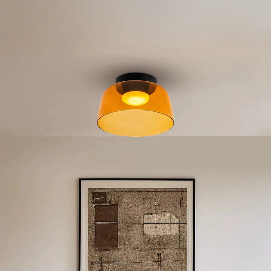 Amber acrylic flush mount light with a warm circular glow above framed artwork in a neutral room.