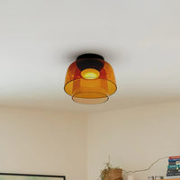 Amber two-tier drum shade ceiling light casting a warm glow above books and a small indoor plant.