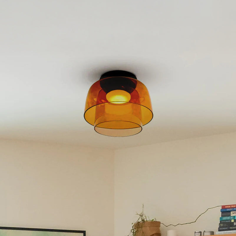 Amber two-tier drum shade ceiling light casting a warm glow above books and a small indoor plant.
