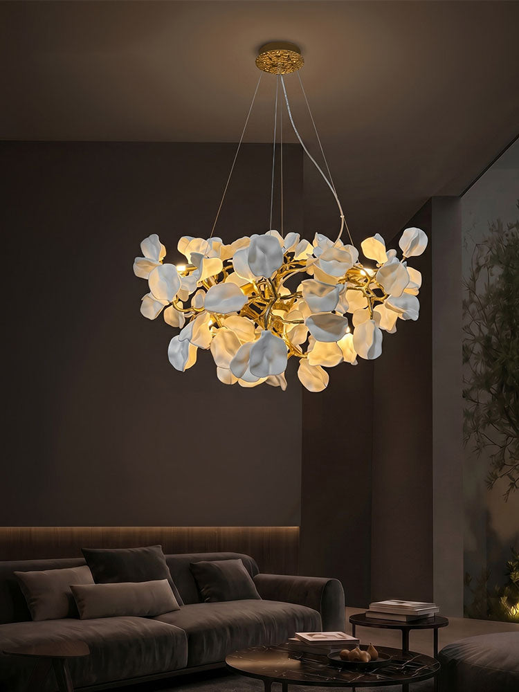 Modern flower chandelier with glowing white ceramic blooms and brass branches in a dark living room.