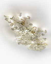 Ceramic flush mount light viewed from below, showing sculpted white ginkgo leaves and a curved gold framework.