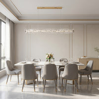 Gold dining room chandelier with a long crystal wave centered above a white dining table in a bright modern dining space.