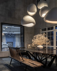 A sculptural dining room chandelier with three wabi-sabi resin shades casting warm pools of light above a dark wood table.