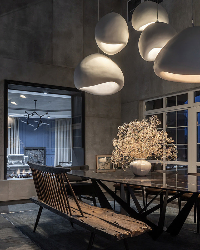 A sculptural dining room chandelier with three wabi-sabi resin shades casting warm pools of light above a dark wood table.