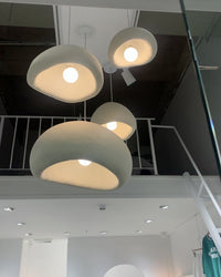 Low-angle view of four sculptural pendants revealing rounded openings, textured resin surfaces and warm bulbs.