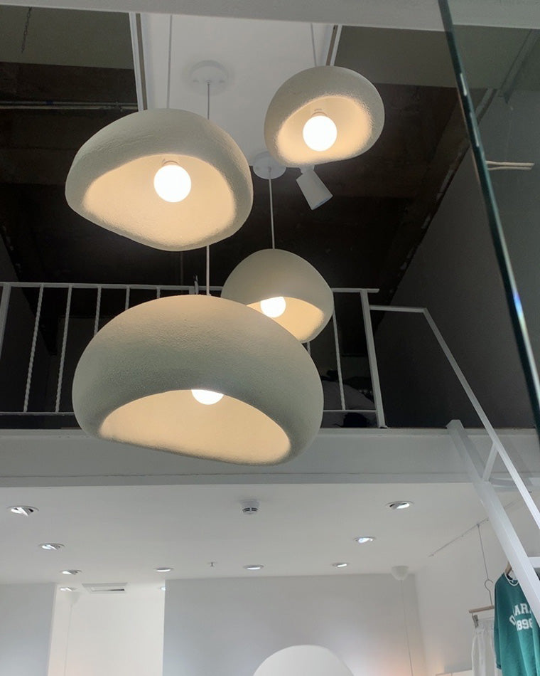 Low-angle view of four sculptural pendants revealing rounded openings, textured resin surfaces and warm bulbs.