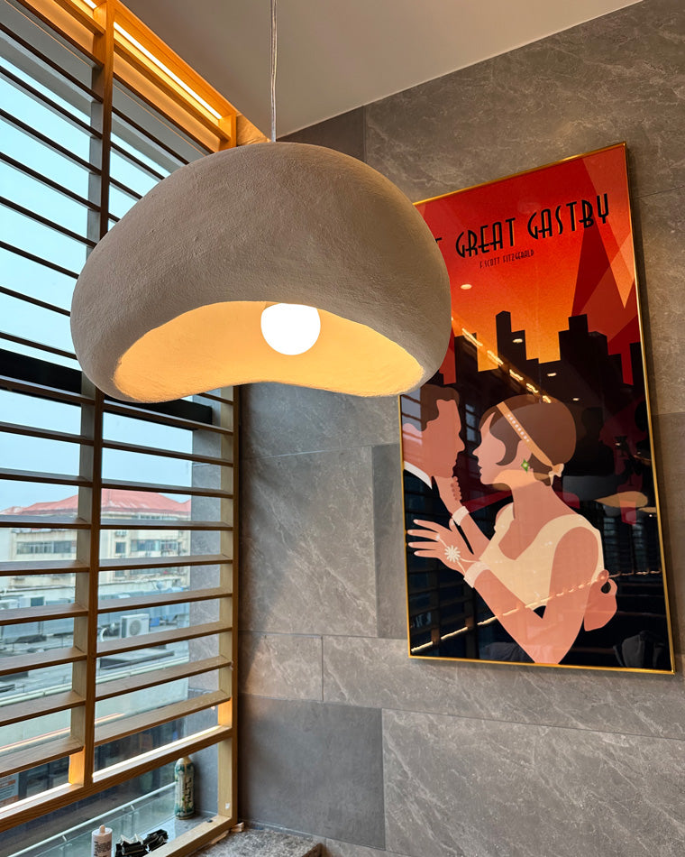 A grey sculptural pendant reveals its warm bulb beside a vivid graphic wall poster.
