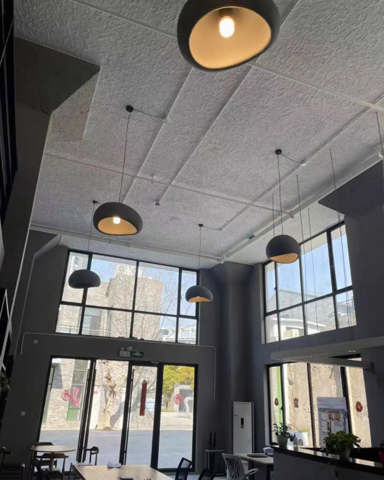 Mixed dome pendants are spaced across an industrial concrete ceiling, balancing hard architecture with rounded forms.