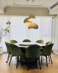 A three-light dining room chandelier adds warm illumination above a round table surrounded by green chairs.