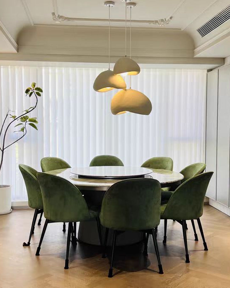 A three-light dining room chandelier adds warm illumination above a round table surrounded by green chairs.
