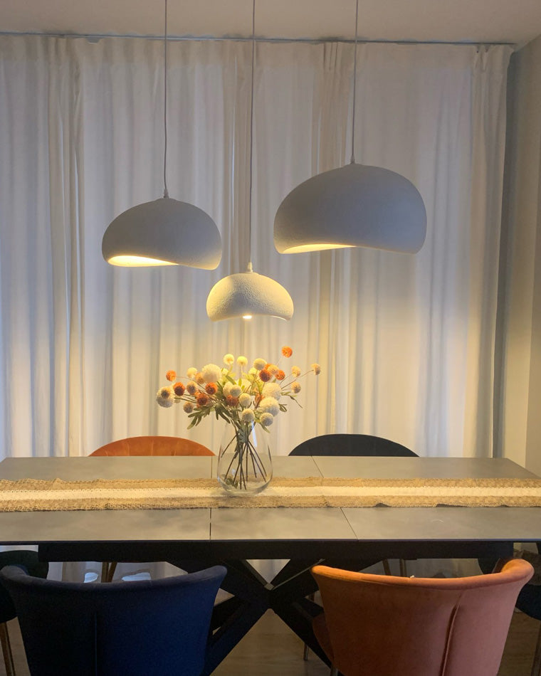 Three resin pendants overlap above a long dining table at dusk, creating depth through varied heights.