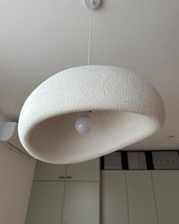 Underside close-up of a white textured resin pendant showing the curved opening and central E27 bulb.