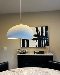 A single white pendant hangs above a dark sideboard and abstract black artwork in a calm interior.