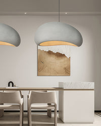 A white dining room chandelier casts warm downward light across a minimalist table, chairs and framed artwork.