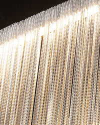 Close-up of illuminated silver chain fringe, revealing the dense texture and softly diffused sparkle behind the chandelier’s rain-like glow.
