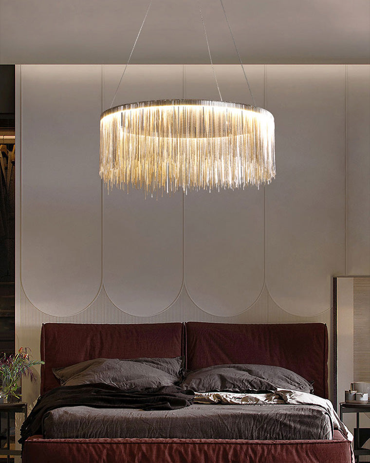 Silver chain-fringe chandelier glowing above a softly layered bed, bringing intimate illumination and polished quiet luxury to the bedroom.