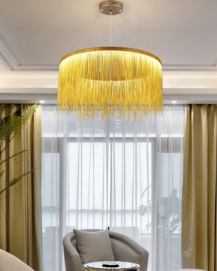 Gold fringe chandelier beside sheer curtains, filtering warm illumination through metallic strands for a sunlit lounge that feels polished after dark as well.
