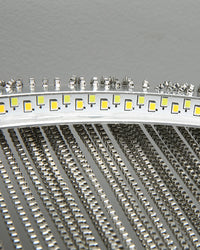 Close-up of the integrated circular light source and silver chain attachments, showing how the slim ring directs illumination through every strand.