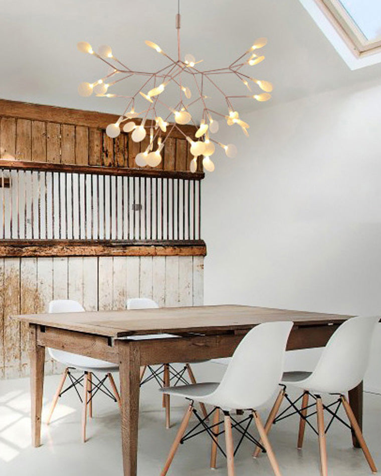Rose-gold Firefly dining light fixture above a natural wood table, turning everyday meals into gatherings beneath a luminous botanical canopy.