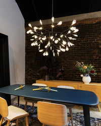 Firefly branch chandelier glowing above a blue dining table, becoming the focal point in interior design against a textured brick wall.