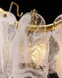 Macro detail of a glass and gold chandelier, showing flowing white swirls inside clear glass, textured surfaces and small gold hooks attached to the curved frame.