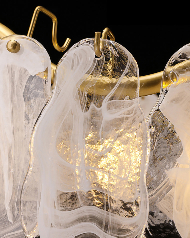 Macro detail of a glass and gold chandelier, showing flowing white swirls inside clear glass, textured surfaces and small gold hooks attached to the curved frame.