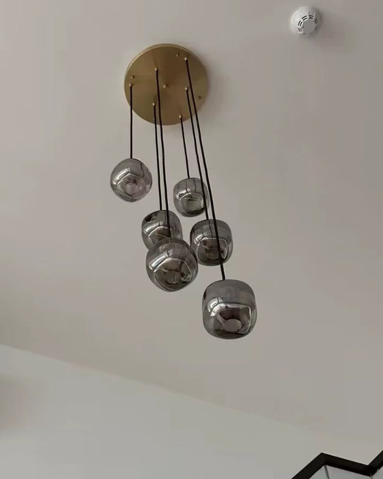 Six smoked glass pendants clustered at varied heights below a warm bronze canopy on a compact cluster pendant chandelier.