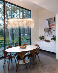 Silver round chandelier illuminating a white dining table beside expansive windows, creating an airy focal point in interior design without blocking the outdoor view.
