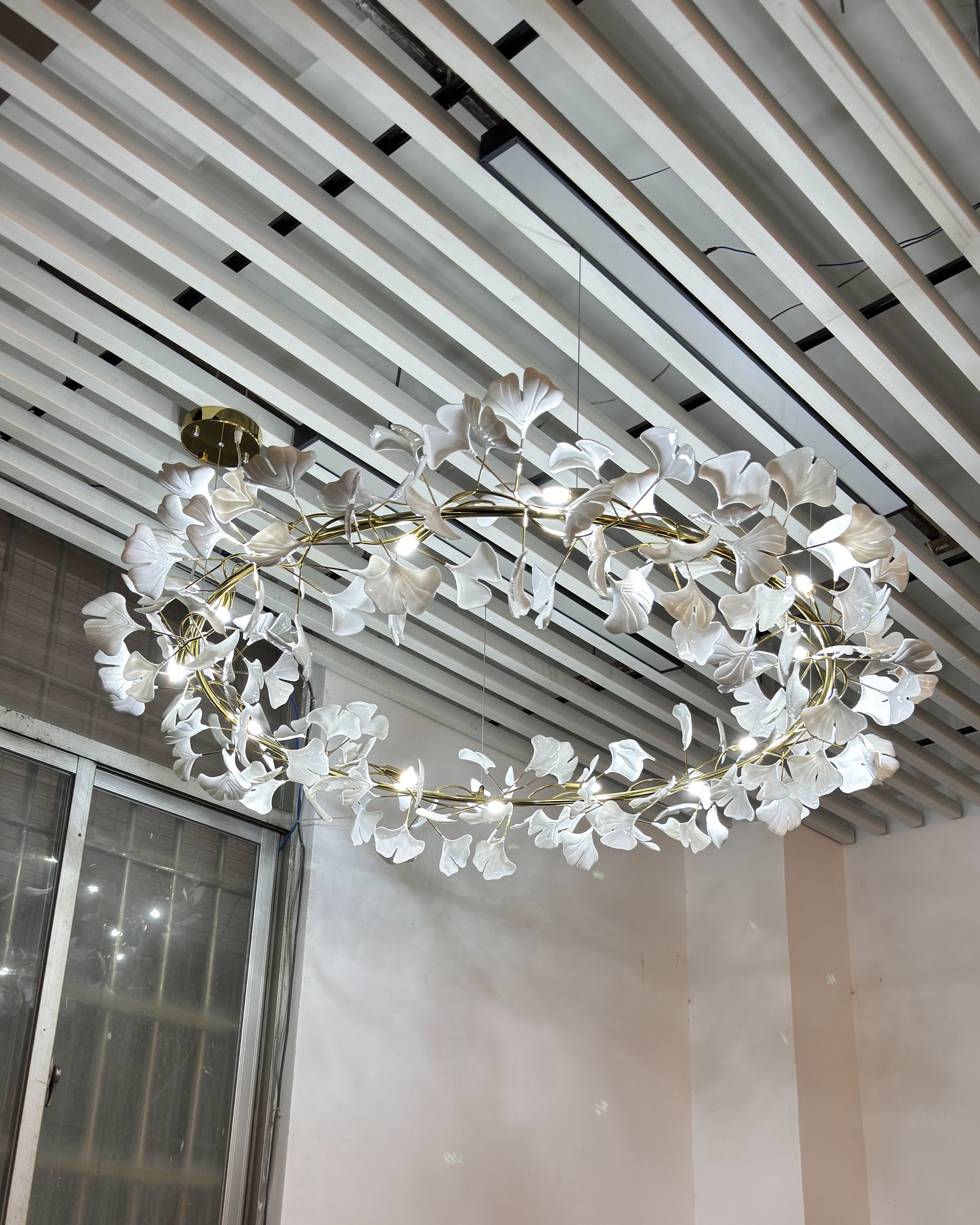Round ceramic leaf chandelier viewed from below beneath a slatted ceiling.