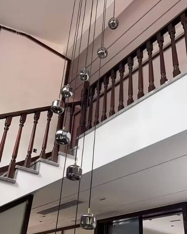 A cascading staircase chandelier beside a dark wood railing in a double-height stairwell, using long cords to draw the eye vertically.