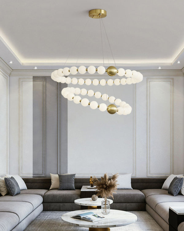 Layered pearl rings bring the refined presence of a visual comfort chandelier above a spacious gray living room, adding light, movement, and jewelry-like elegance.